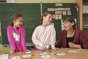 Eine Lehrperson unterstützt zwei Kinder bei einer spielerischen Übung mit Zahlen.