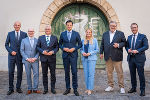 Gruppe von sieben Personen in formeller Kleidung steht vor einer verzierten Tür.